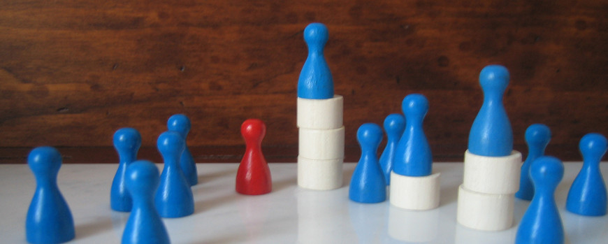10 blaue und eine rote Spielfigur stehen auf einer Unterlage. Drei blaue Spielsteine stehen erhöht auf unterschiedlich hohen weißen Türmen.