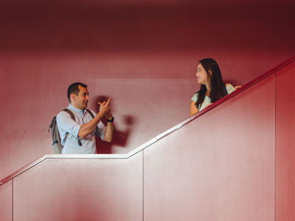 Mann und Frau stehen auf einer roten Treppe und sprechen miteinander.