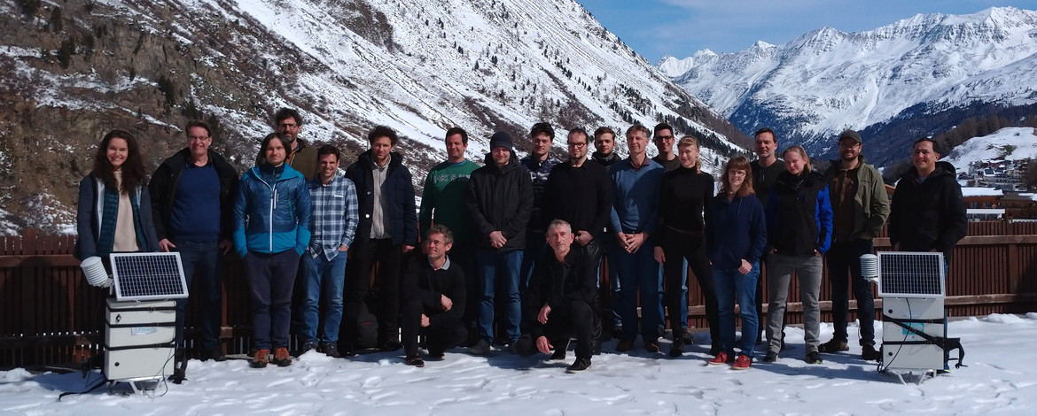 Gruppenfoto des Cosmic Sense Teams: 21 Personen und zwei mobile CRNS Sensoren vor einer winterlichen Alpenlandschaft. Aufgenommen im April 2023 in Obergurgl (Österreich) | Foto: Cosmic Sense Konsortium - 