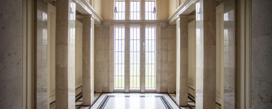 Großes, mehrstöckiges Foyer aus Marmor mit hohen Fenstern im Hintergrund