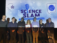 Sieben Personen vor beleuchteter Leinwand mit der Aufschrift Science Slam