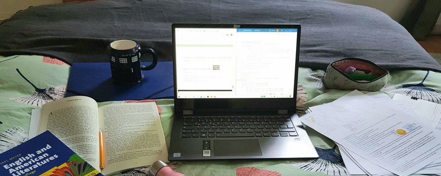Laptop, Bücher und Schreibsachen auf einem Bett