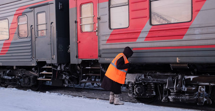Anschnitt eines rot/grauen Zuges im Schnee, davor ein Mensch, der an den Rädern des Zuges arbeitet.