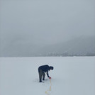 Field site Leutasch: Scientist laying out measuring tape in the snow, with faint silhouettes of mountains in the foggy background | Photo: Cosmic Sense Consortium