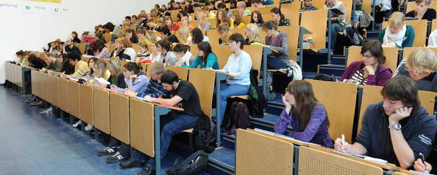 Die Reihen eines Hörsaals sind zu sehen. In den Reihen des Hörsaals sitzen viele Student:innen