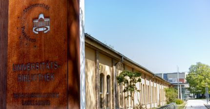 Flaches, langgestrecktes Gebäude, links im Vordergrund Metallsäule mit Schriftzug "Universitätsbibliothek Bereichsbibliothek Babelsberg"