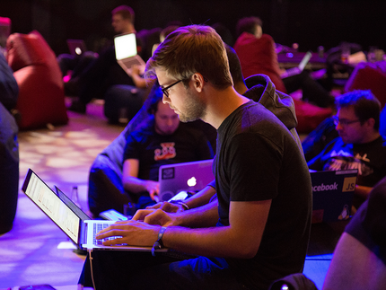 junger Mann sitzend mit Laptop auf dem Schoß auf einer Digital-Konferenz