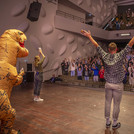 zwei Personen und ein aufblasbarer T-Rex auf einer Bühne, im Hintergrund Zuschauende