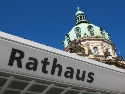 Im Vordergrund das Haltestellenschild "Rathaus", im Hintergrund die Kupferkuppel des Rathauses