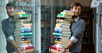 Student trägt Bücherstapel in der Bibliothek, Foto: Thomas Roese