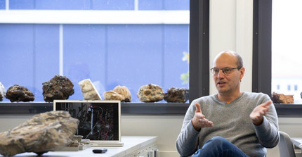 Professor Wilke im Gespräch vor Gesteinsmustern und Bildschirm erläutert seine Forschung