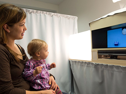Mutter und Kind blicken auf einen Bildschirm, darunter ist ein Eye-Tracker befestigt