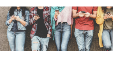 Fünf junge Menschen stehen nebeneinander an eine Hauswand gelehnt mit Smartphones in den Händen. Sie sind von den Knien bis zum Hals zu sehen.