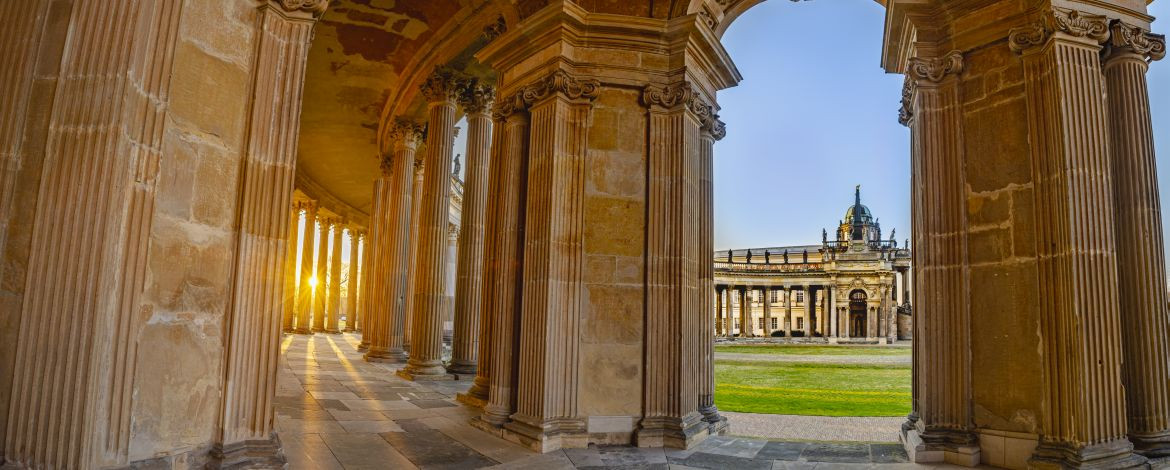 Blick aus einem halbrunden Säulengang auf ein historisches Nebengebäude des Neuen Palais - 