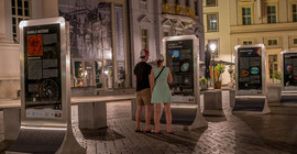 Zwei Personen sehen sich die Ausstellung auf dem Potsdamer Alten Markt bei Nacht an.