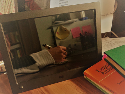 Digitaler Bilderrahmen mit Spieglung von schreibender Hand auf Schreibtisch