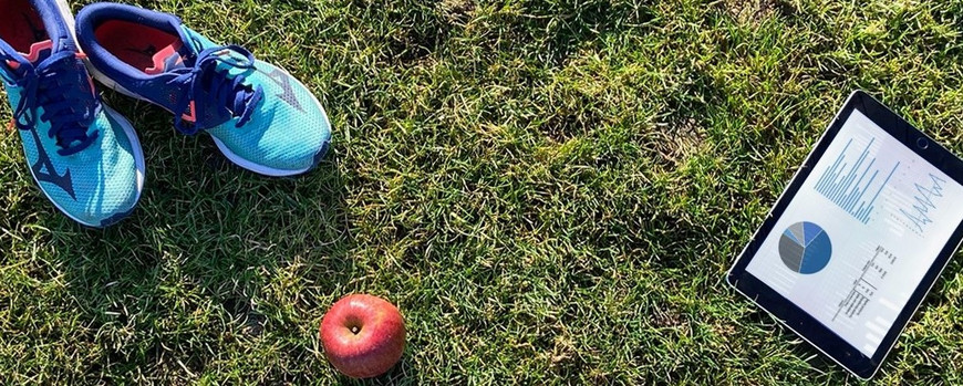 Sportschuhe, Apfel und Tablet auf grüne Wiese