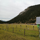 Field site Esterberg: A bright green CRNS sensor with solar panel standing on a green pasture with forested hills in the background | Photo: Cosmic Sense Consortium
