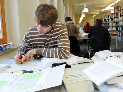 Ein Studierender sitzt in der Bibliothek an einem Tisch und recherchiert.