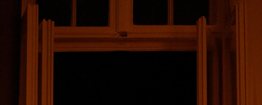 Laptop mit Lampe vor offenem Fenster in der Nacht