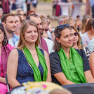 Mehrere Personen in festlicher Kleidung und mit bunten Schals sitzen in Reihen