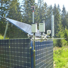 Foto: A cube of solar panels containing a gravimeter with other measuring equipment attached to it, with forest in the background | Foto: Cosmic Sense consortium