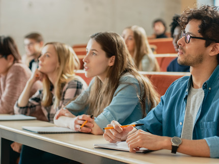 Studierende sitzen im Hörsaal, hören zu und machen Notizen.