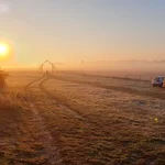 Der Blick von den Gebäuden auf das Eingangstor der Station im Morgenlicht. Raureif hat sich aufs Gras gelegt und glänzt im Morgenlicht.