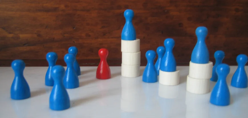 10 blaue und eine rote Spielfigur stehen auf einer Unterlage. Drei blaue Spielsteine stehen erhöht auf unterschiedlich hohen weißen Türmen.