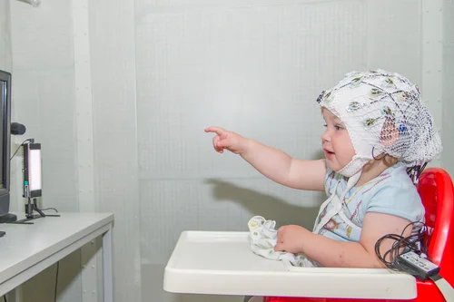 Kind mit EEG-Kappe auf dem Kopf zeigt auf einen Bildschirm