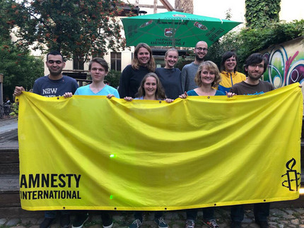 mehrere Personen halten die gelbe Flagge von Amnesty International
