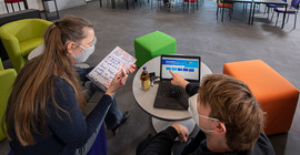 Prof. Lucke und Mitarbeiter sitzen am Tisch und arbeiten, Person rechts zeigt auf einen Laptop. Das Foto ist von Thomas Roese.