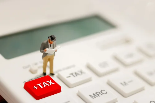 Eine Figur steht auf einem Taschenrechner auf dem das Wort "Tax" hervorgehoben ist