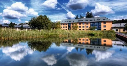 In einem Feuerlöschteich spiegeln sich der Himmel und im Hintergrund ein Haus