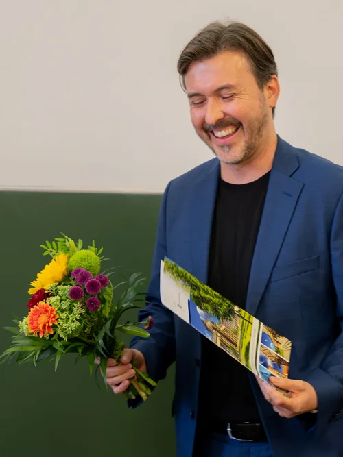 Alex Kay mit Blumen und Urkunde zur bestandenen Habilitation