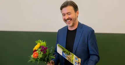 Alex Kay mit Blumen und Urkunde zur bestandenen Habilitation