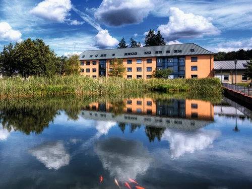 In einem Feuerlöschteich spiegeln sich der Himmel und im Hintergrund ein Haus