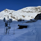 Field site Dresdner Hütte: Measuring equipment installed at a hillslope and the chalet Dredner Hütte in winter, with rocky mountain top in the background | Photo: Cosmic Sense Consortium