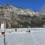 Field site Graswang: Laser scanner on a tripod standing on a flat valley bottom with snow and forested mountains in the background. Several scientists are working with different equipment in the valley. | Photo: Cosmic Sense Consortium
