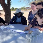 NamTip researchers jointly looking at a map opened on the bonnet of a 4x4 car and in the shade of a tree