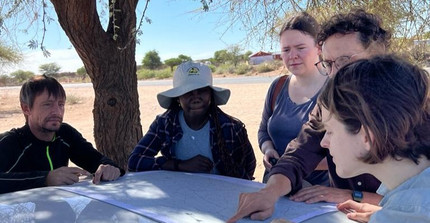 NamTip researchers jointly looking at a map opened on the bonnet of a 4x4 car and in the shade of a tree