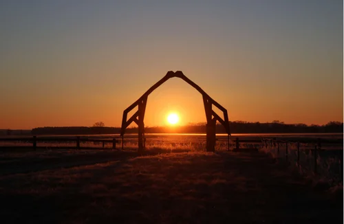 Sunrise seen through a gate whoch looks like two cranes