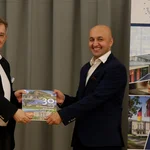 Prof. Florian Schweigert gratuliert Najibullah Kakar. Beide halten zusammen ein Buch über die Universität potsdam in die Kamera.