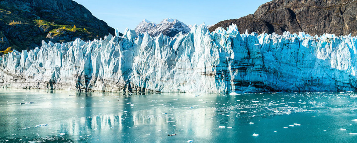 Eine Gletscherfront, die bis ans Wasser im Vordergrund ragt. Im Hintergrund Bergformationen. - 