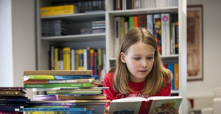 Schülerin sitzt vor einem Stapel Schulbücher und liest