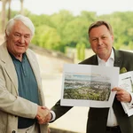 Zwei Männer reichen sich die Hände, einer hält ein Foto ins Bild