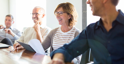 Dekoratives Bild von 4 Erwachsenen, die an einem Tisch sitzen und arbeiten