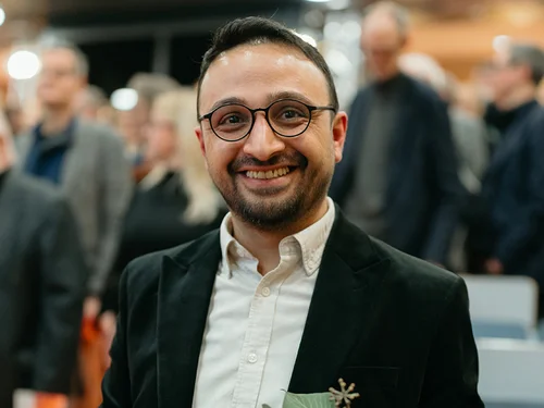 Ein Mann steht mit Blumenstrauß und Auszeichnung in einem Hörsaal