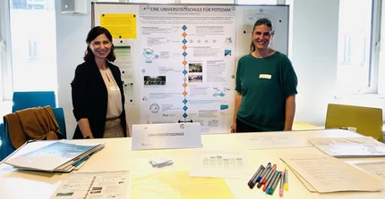 Das Bild zeigt Mitarbeiterinnen der Universitätsschule vor ihrem Stand beim Markt der Möglichkeiten im Rahmen der Veranstaltung "Uni trifft Schule".