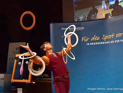 Ein Mann mit roter Weste jongliert mit Ringen vor einer blauen Wand